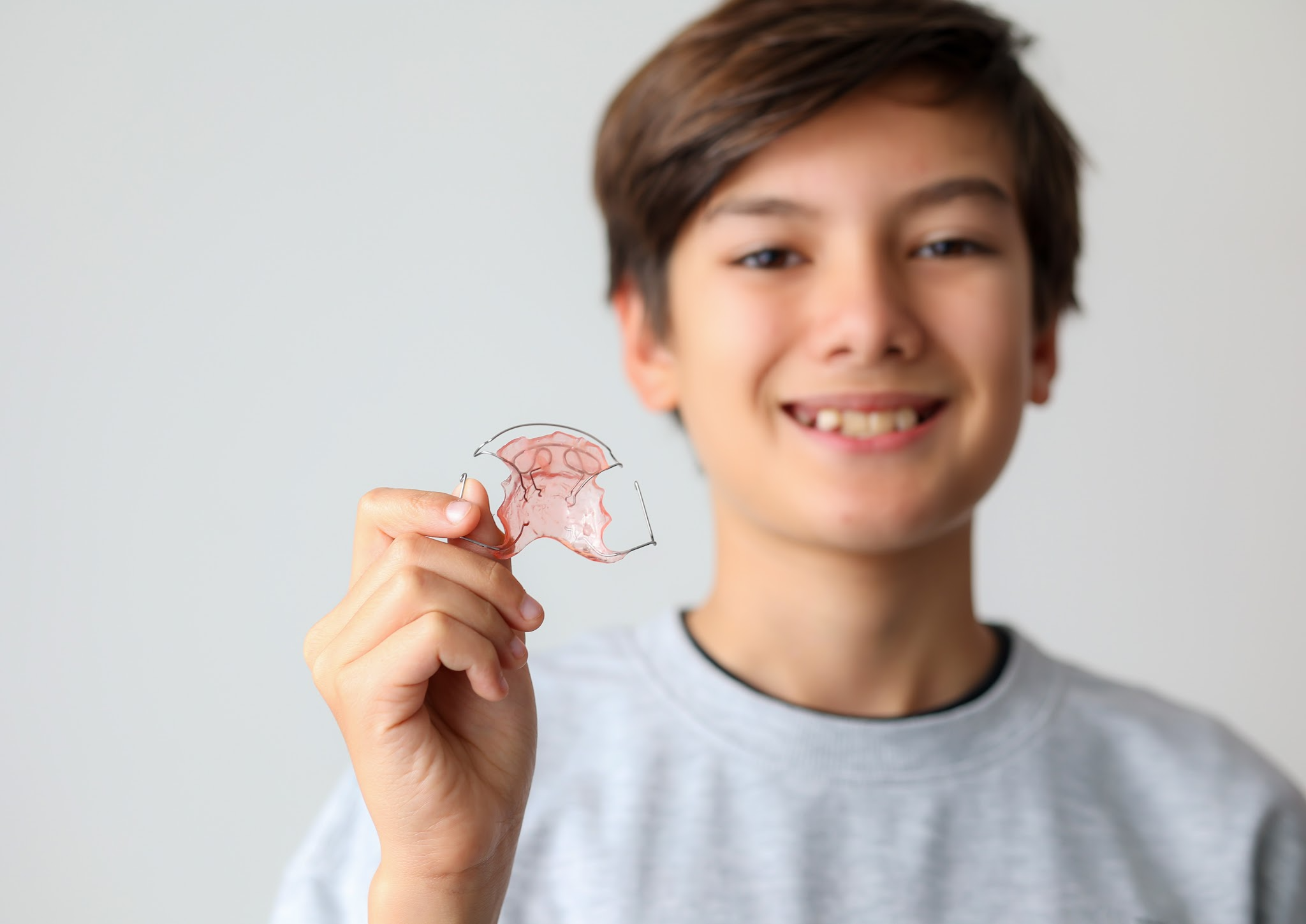 Junge im Grundschulalter hält eine herausnehmbare Zahnspange in der Hand
